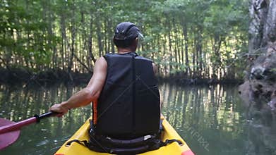old man paddles on kayak in canyon among mangrove jungle