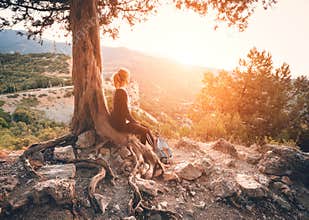Young woman sitting on the mountain at sunset. Summer landscape