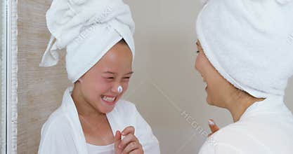 Happy mother and daughter playing with face cream