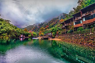 Wooden lodge buildings beside calm green lake, mountain forest autumn scenery, Guniujiang Anhui China
