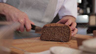 Cook Cuts a Slice of Bread on a Cutting Board with a Knife