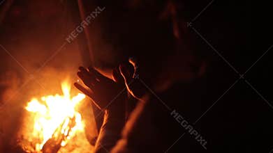 Man heats hands at burning bonfire. Summer night. Camping