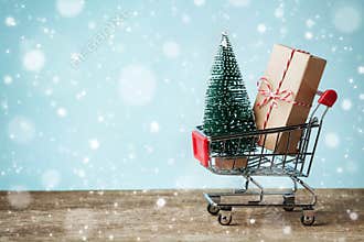 Shopping cart with gift or present and fir tree on snowy effect background. Christmas and New year sale concept. Greeting card.