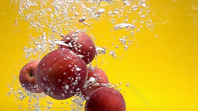 Whole red apples falling under water