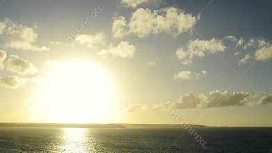 Wide shot of a sunset in timelapse over the ocean and cliffs on the horizon. Zooming progressively on the cliffs.