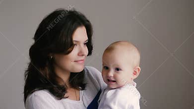Young Happy Mother Holding her Newborn Child. Family at home. Beautiful smiling Mom and Happy Baby Together.