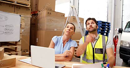 Warehouse workers using laptop and pointing shelves