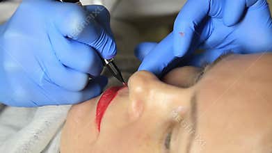 Cosmetologist applying permanent make-up. Young beautiful woman having cosmetic tattoo on her lips. Healthy Spa