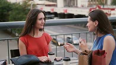 Beautiful women drinking coffee communicate in a cafe with a view of the traffic, talking after shopping. 4k