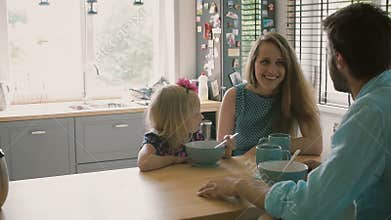 Husband is talking to his smiling wife while their daughter is having breakfast. Slow motion