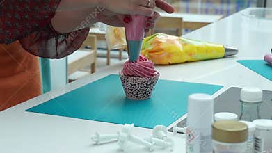 Decorating colorful cupcake with whipped cream and sprinkles. Women putting sprinkles on the tasty muffin.