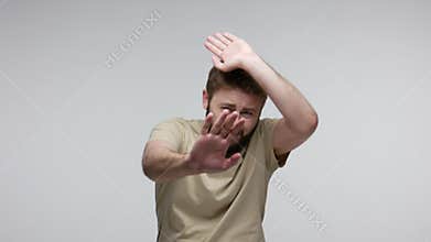 Scared bearded man walking back raising hands to defend against threat danger, afraid even look at phobia