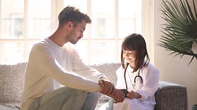 Preschool daughter wearing white coat uniform playing doctor with father