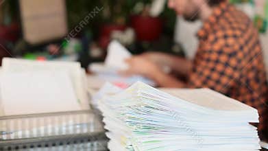 A man parses papers in the office and stacks them in a pile. Focus on a stack of papers.