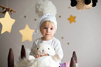 Cute child, blonde boy, playing at night with colorful scarf and teddy bear in clouds and stars