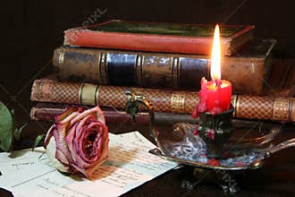 Withered rose with candle flame and antique book