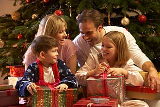 Family Opening Christmas Present In Front Of Tree