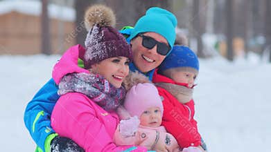 Joyful man hugs wife and children sitting on snow closeup