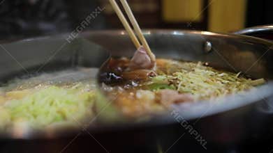 Shabu-Shabu or Sukiyaki, Japanese or Chinese Traditional Food. a Woman Dipping Sliced Pork in Hot Pot by Chopstick. Slow Motion