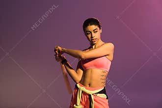 African american girl in pink sports bra holding baseball bat on purple background