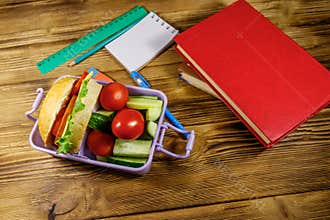 Back to school concept. School supplies, books and lunch box with burgers and fresh vegetables on wooden table
