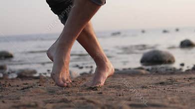 Barefoot men`s feet dance on the sand by the sea