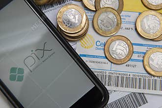 Florianopolis, Brazil. 07/10/2020: Close up of PIX logo on smartphone screen and coins over bills and bills to pay with barcode.
