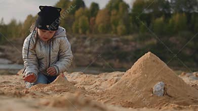 The girl sits on the sandy shore and builds a sand castle.