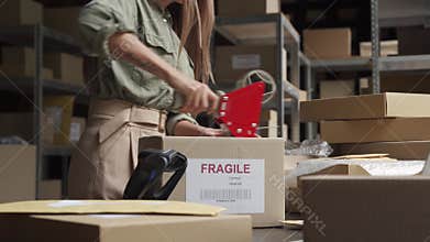 Female post mail storage worker holding tape dispenser sealing shipping box.