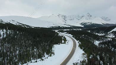 Aerial footage of black forest, white rocky mountains, winter road Alberta, Canada