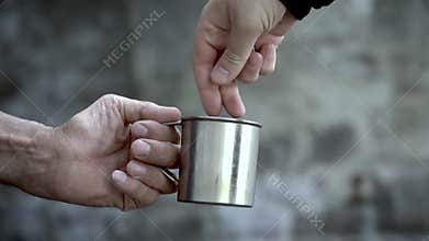 Distribution of coins to a beggar. Businessman gives money to a homeless old man in a metal mug. Helping hand. Close-up