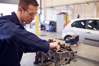 Female Student Works On Car Engine Block On Auto Mechanic Apprenticeship Course At College