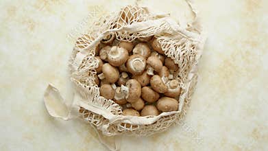 Young fresh Champignons in a ecological zero-waste net bag placed on beige background
