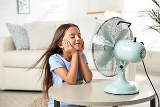 Little girl enjoying air flow from fan. Summer heat