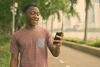 Happy young handsome African man using phone at the park