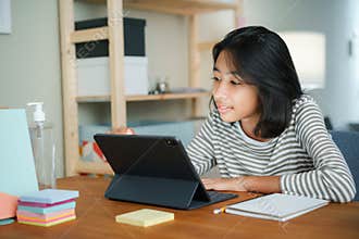 Asian girl is studying online via the internet on tablet digital while sitting at the table at night. Concept of online learning