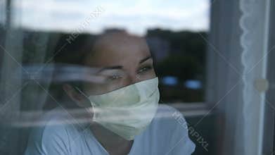 Young woman wears a mask to protect herself from covid-19 while looking out the window. slow motion