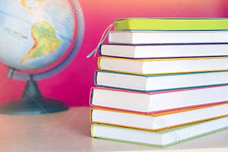 Stack of colorful books and globe, bright colorful pink background, free copy space. Books on table, no labels, blank spine. Back