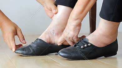 Elderly woman swollen feet putting on shoes with care giver