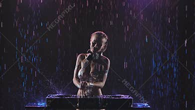 Sexy nude blonde dj with shiny bodypainting on the body control sound console for mixing music in dark studio under