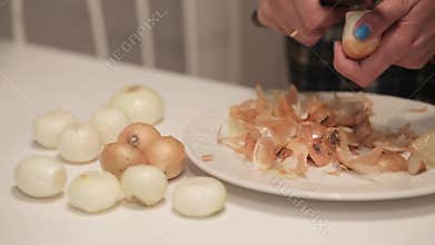 Female hands peeling onion on white table. the cook peels the onion over the tabl.