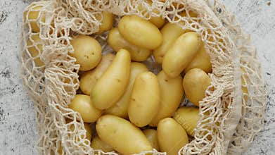 Young fresh Potatoes in a ecological zero-waste net bag placed on white scratched background