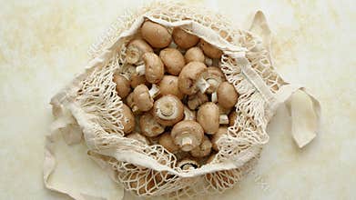 Young fresh Champignons in a ecological zero-waste net bag placed on beige background