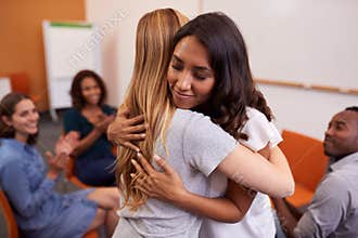 Two Women Hugging As Group Of Men And Women At Mental Health Group Therapy Meeting