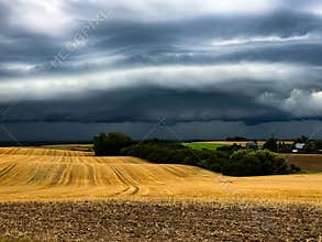 Dark cumulonimbus clouds bringing heavy rain over harvested agrarian fields