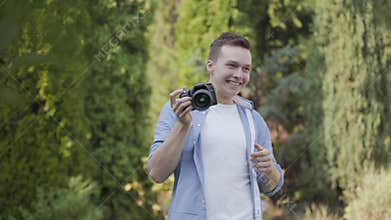 Young professional male photographer in casual clothes taking photo with his camera in the park or garden. Photography