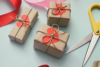 Process of packaging gift boxes. Thanks gifts. Wedding presents. Pink ribbon and yellow scissors. Red carton hearts.