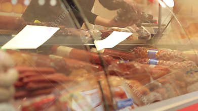 Closeup of female butcher`s hand displaying sausage in shop