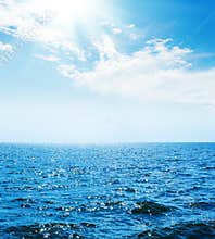 blue sea with waves and sky with sun and clouds