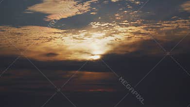 Orange sun shines beautifully behind dramatic clouds in the blue sky